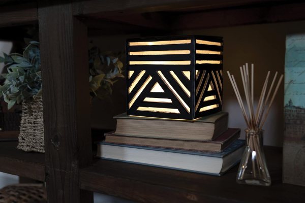 Geometric table lamp with black and white stripes on a wooden shelf.