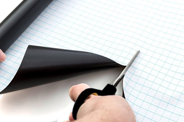 Person applying black chalkboard sticker on graph paper with scissors.