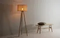 Elegant wooden tripod floor lamp with warm light in minimalist space.