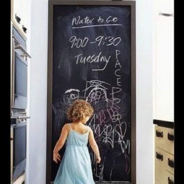 Child drawing on blackboard with chalk in a classroom setting.
