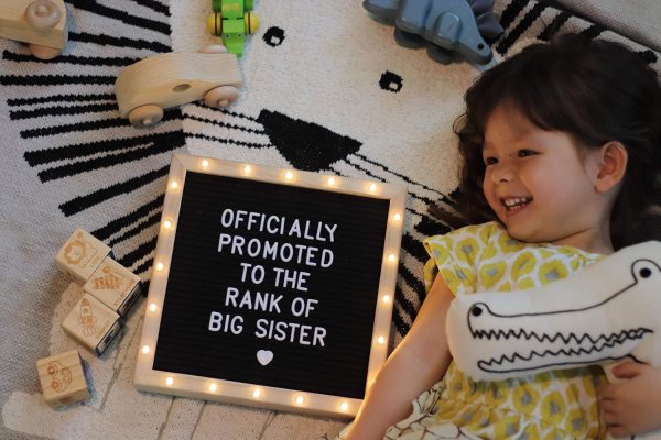 Kids with LED message board displaying 'Officially promoted to big sister'.