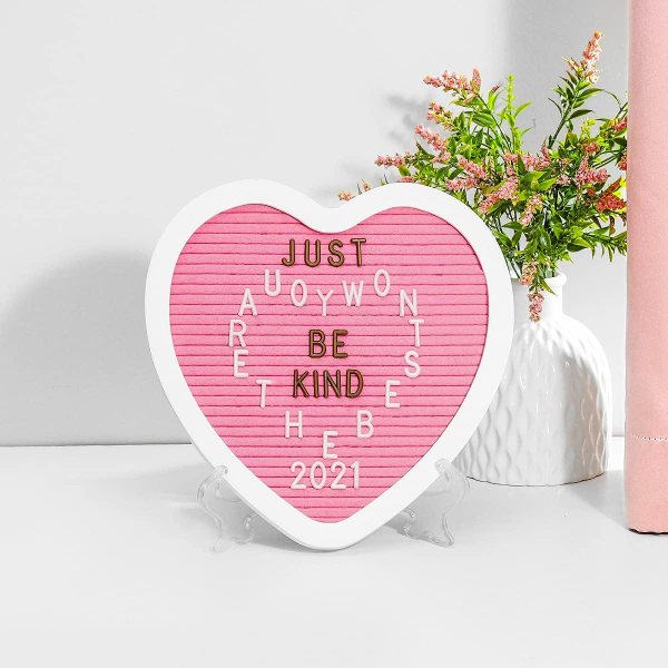Heart-shaped letter board with motivational message and flowers in background.